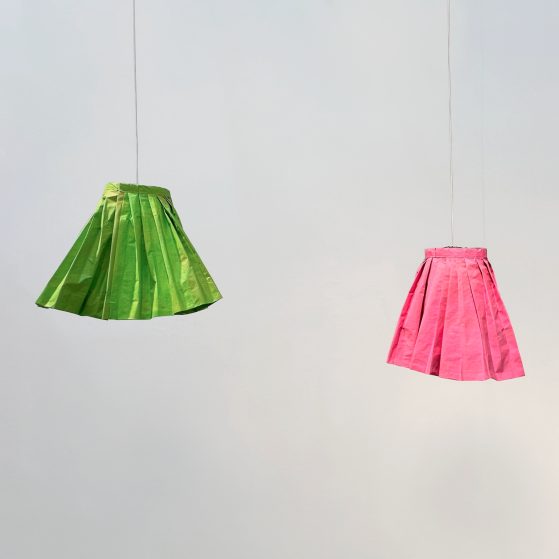 Paper sculptures of a green and a pink skirt hanging on the wall