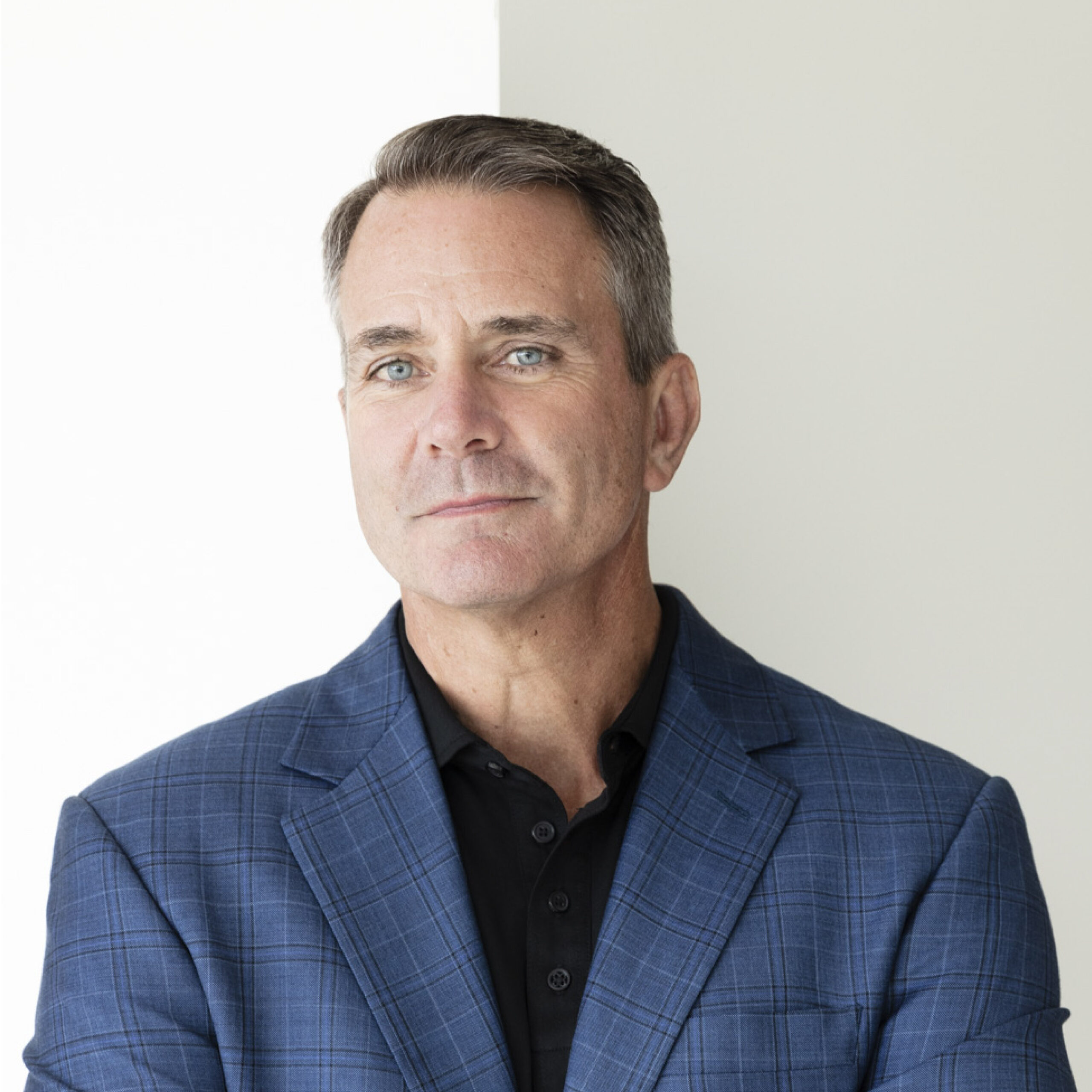 A professional headshot of Ray Scott, president and CEO of Lear Corp., wearing a blue plaid suit jacket over a black button shirt. 