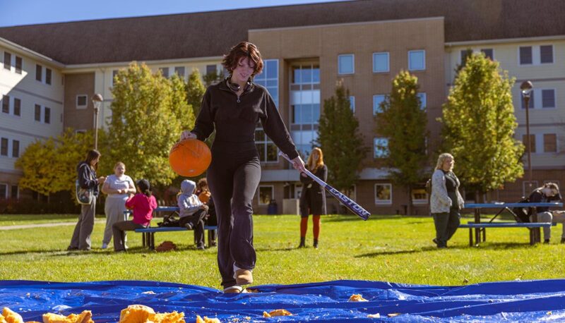 A student smashing pumpkins with a baseball bat.