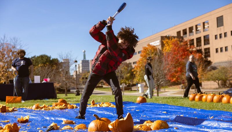 A student smashing pumpkins with a baseball bat.