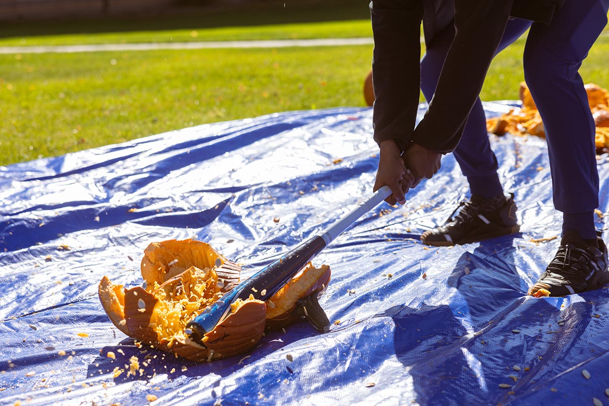 A closeup of a student smashing a pumpkin with a baseball bat.