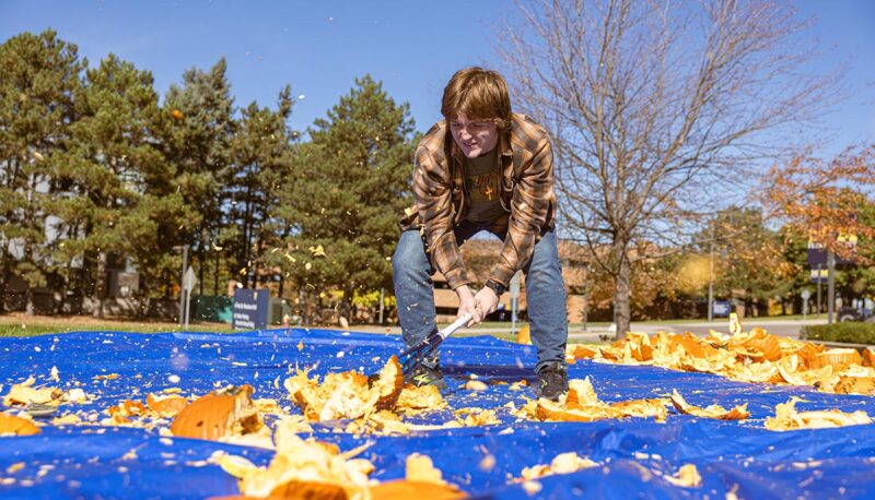 A student smashing pumpkins with a baseball bat.