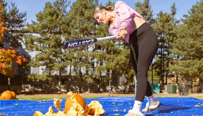 A student smashing pumpkins with a baseball bat.