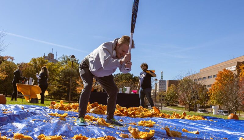 A student smashing pumpkins with a baseball bat.