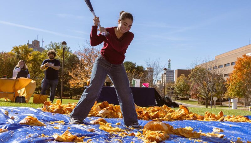 A student smashing pumpkins with a baseball bat.