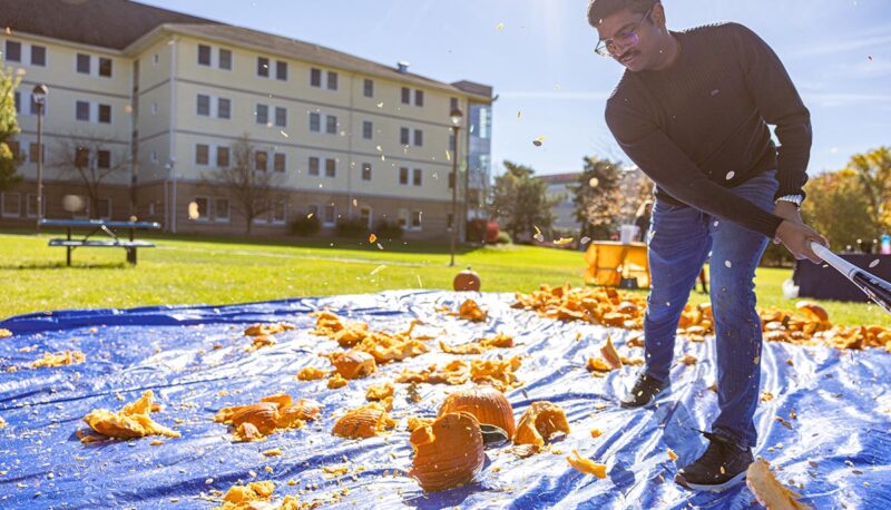 A student smashing pumpkins with a baseball bat.