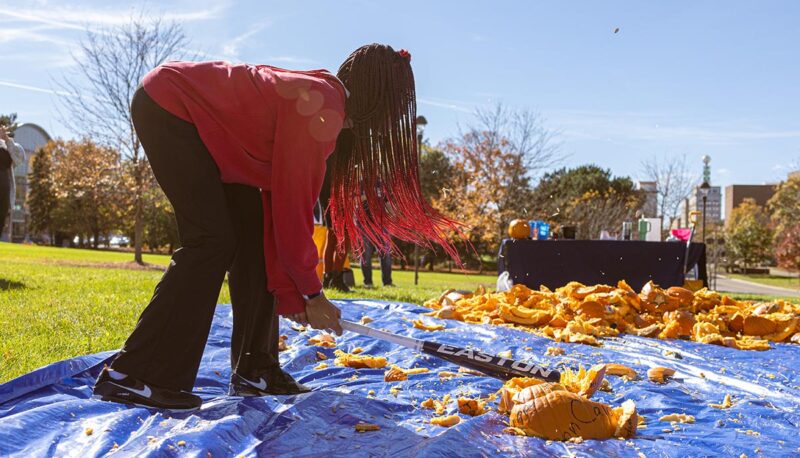 A student smashing pumpkins with a baseball bat.