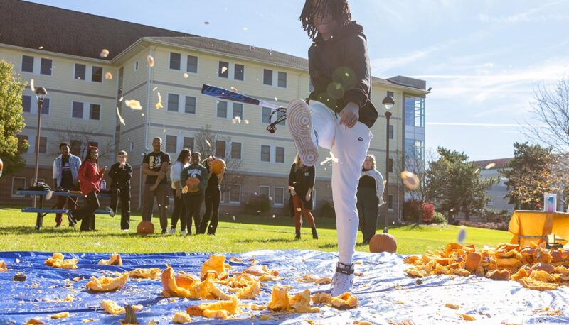 A student smashing pumpkins with a baseball bat.