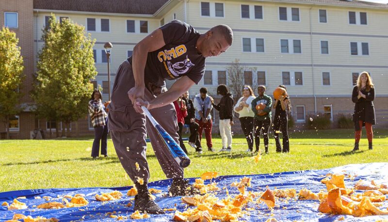 A student smashing pumpkins with a baseball bat.