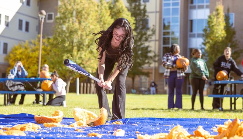 A student smashing pumpkins with a baseball bat.