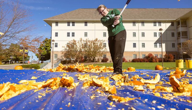 A student smashing pumpkins with a baseball bat.