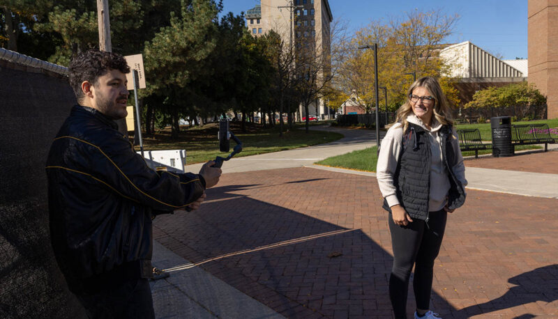 A cameraman filming a student outside the William S. White Building