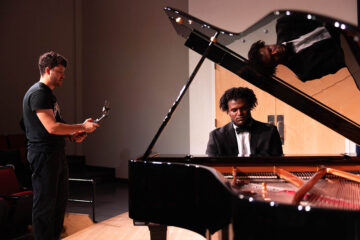 A student in a tuxedo playing the piano being filmed.