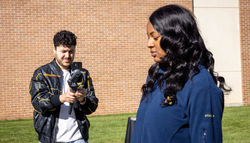 A student walking outside on campus being filmed