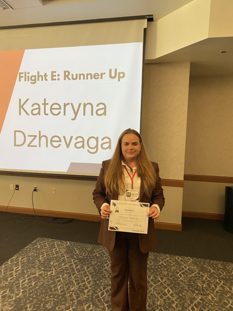 UM-Flint School of Management Marketing Student Kateryna Dzhevaga poses infront of a large screen with her runner-up award at SVSU Regional Sales Competition on Oct. 11-12. 