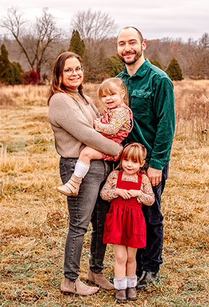 A mother and father with their two small daughters posing for a family picture in a field