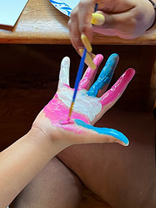 A child's hand being painted in pink, white, and blue as part of an art therapy activity.