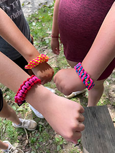 Three children's hands showing the multi-colored bracelets they wove themselves