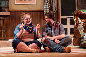 Two students sitting cross-legged on stage while performing. 