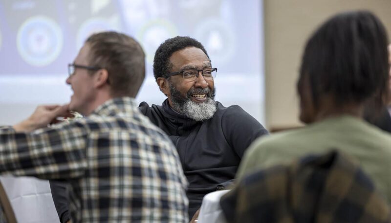 A man smiling while seated in the crowd.