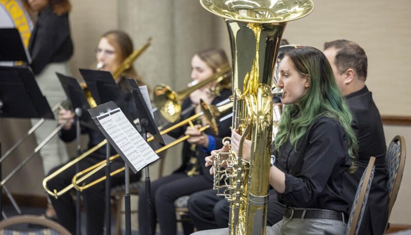 A student playing a tuba along with other brass ensemble members behind.