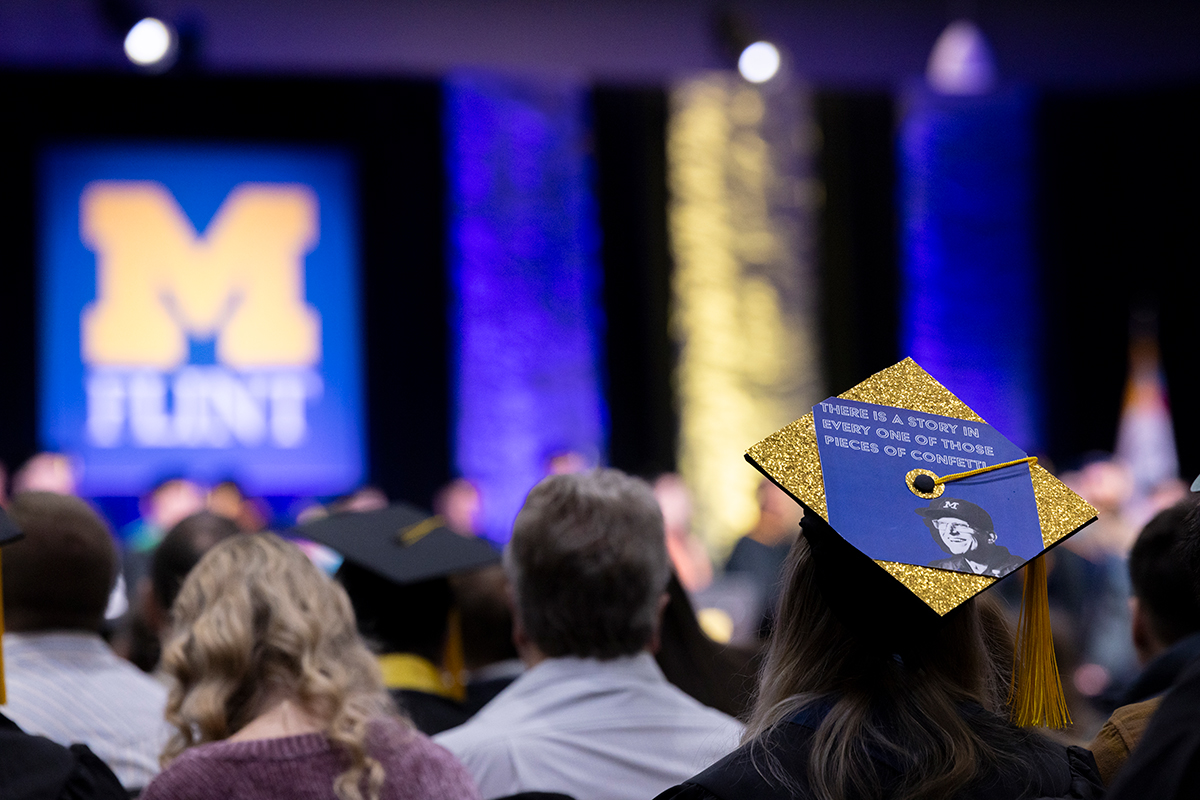 A decorated graduation cap with gold glitter and a quote about confetti, worn at a commencement ceremony.