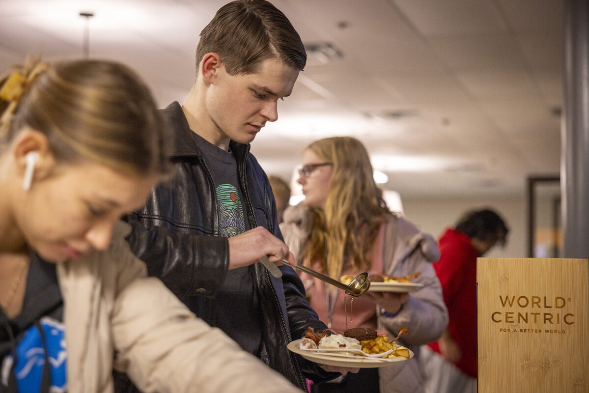 A person serving himself breakfast from a buffet while others wait in line.