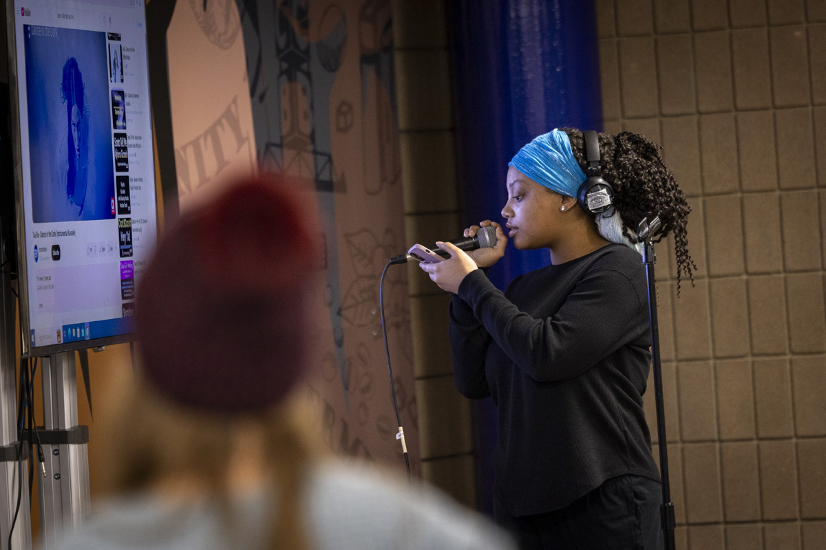 A young person sings into a microphone while wearing headphones.