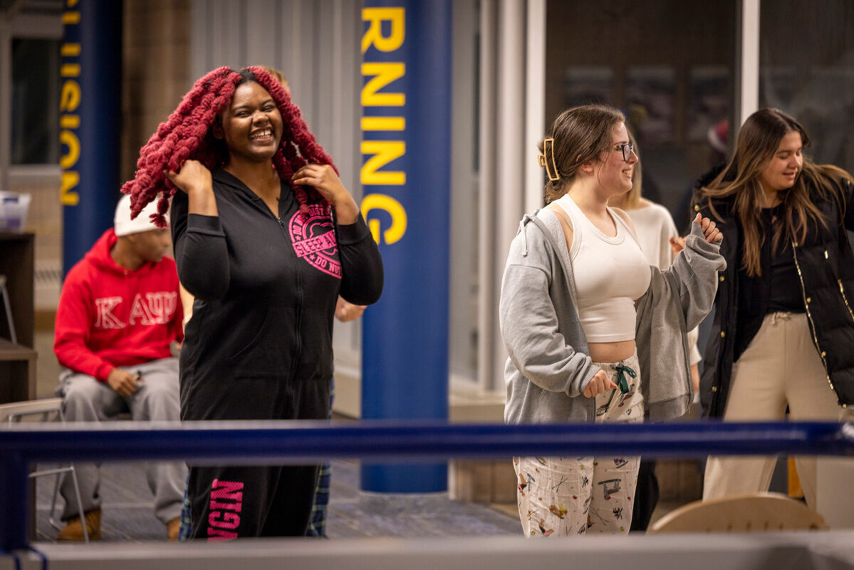 A group of people smiles and dances in a brightly lit indoor setting, with casual and colorful attire.