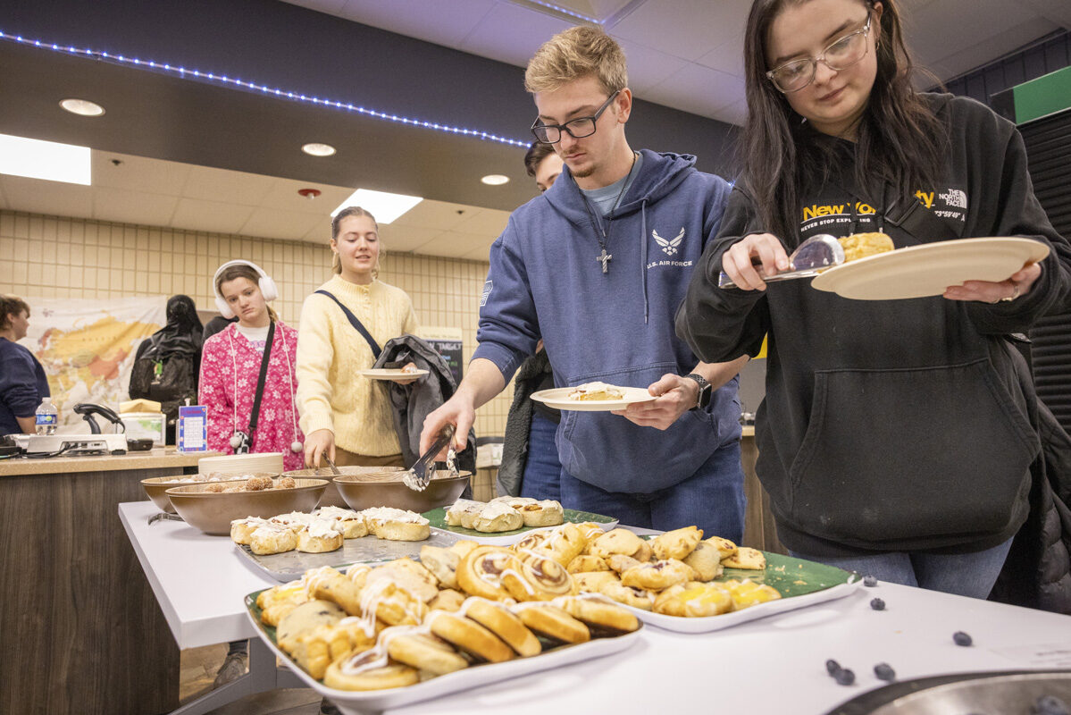 A group of people serving themselves pastries from a breakfast buffet table.