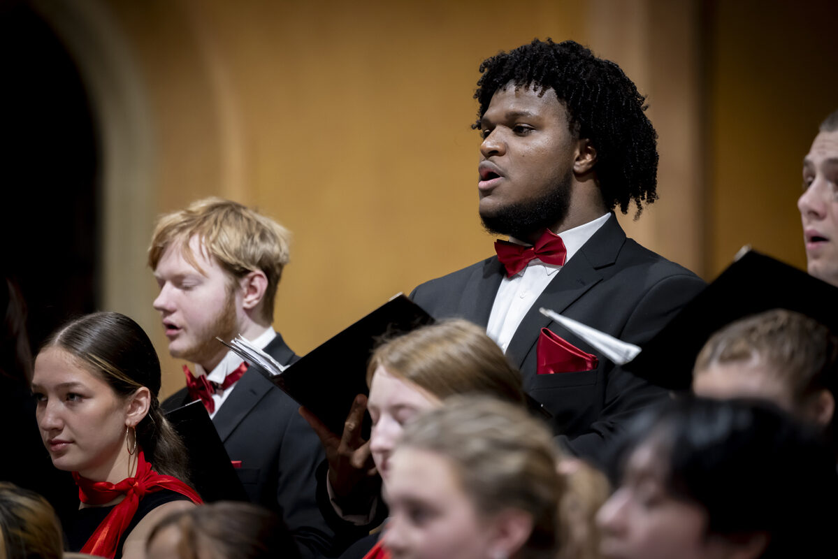 A close-up of choir members singing, wearing formal black attire with red accents.