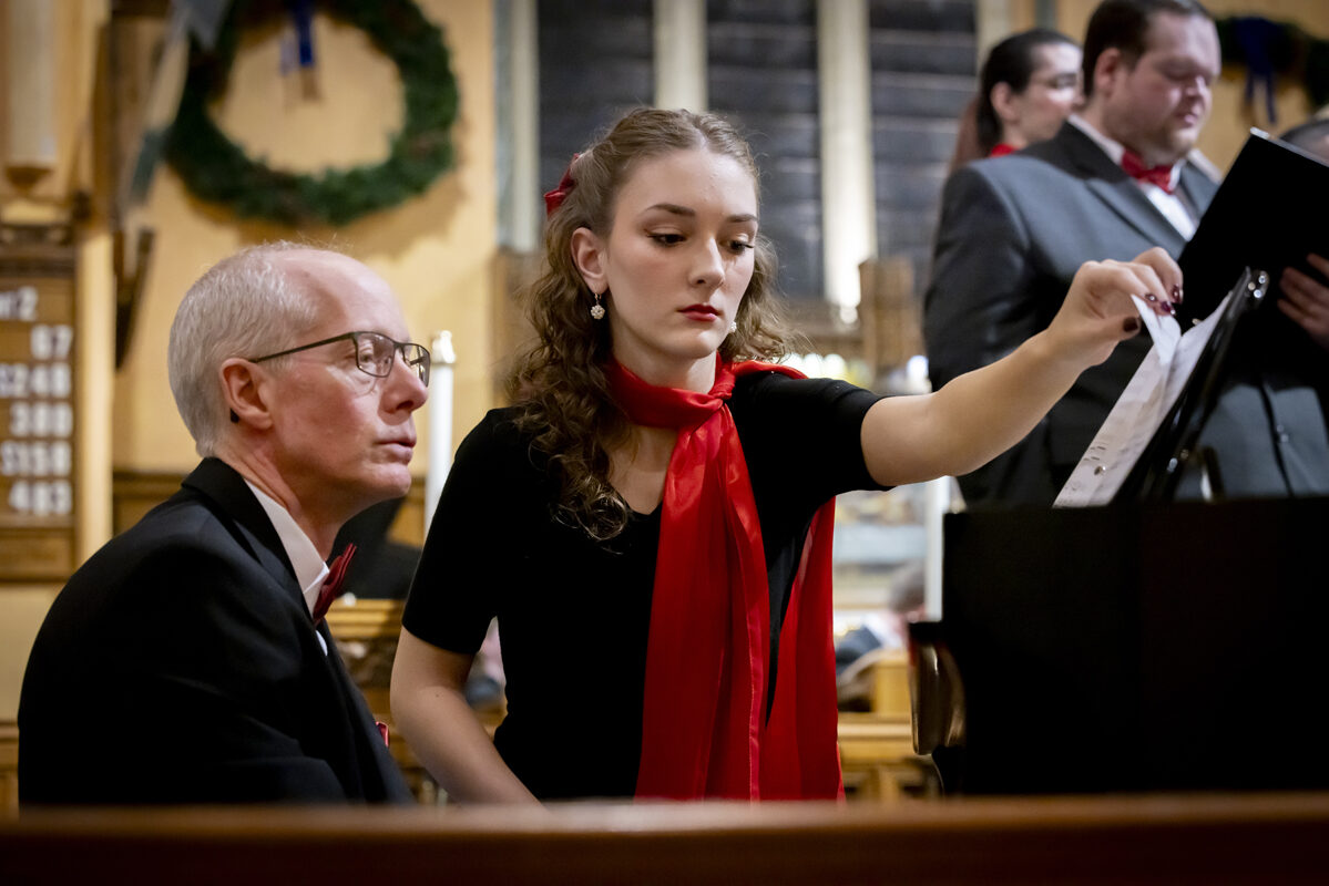 A young woman adjusts a music sheet while a man watches.