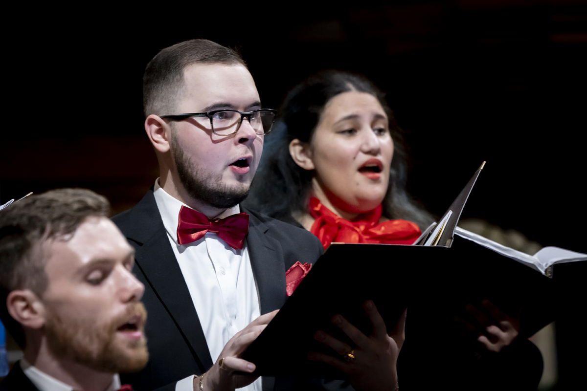 Two singers perform, holding music folders.