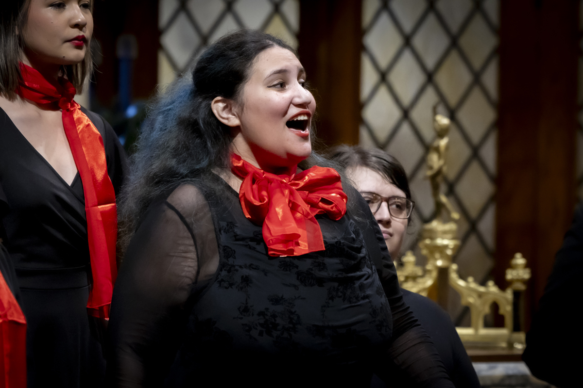 A woman sings with passion, wearing a red scarf.