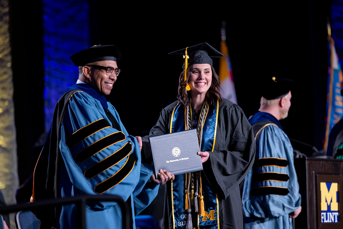 A graduate shakes hands with a faculty member while holding her diploma.