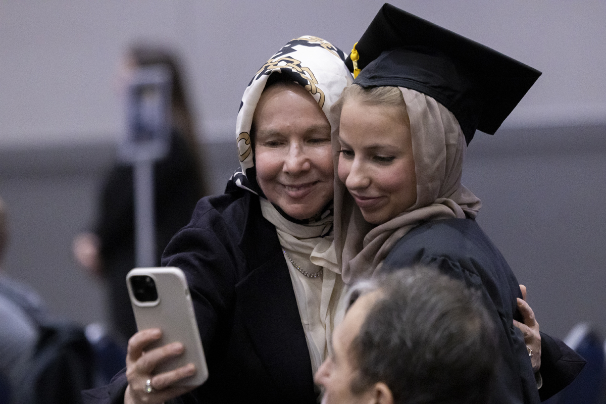 Two women, one in a headscarf and graduation cap, pose for a selfie.