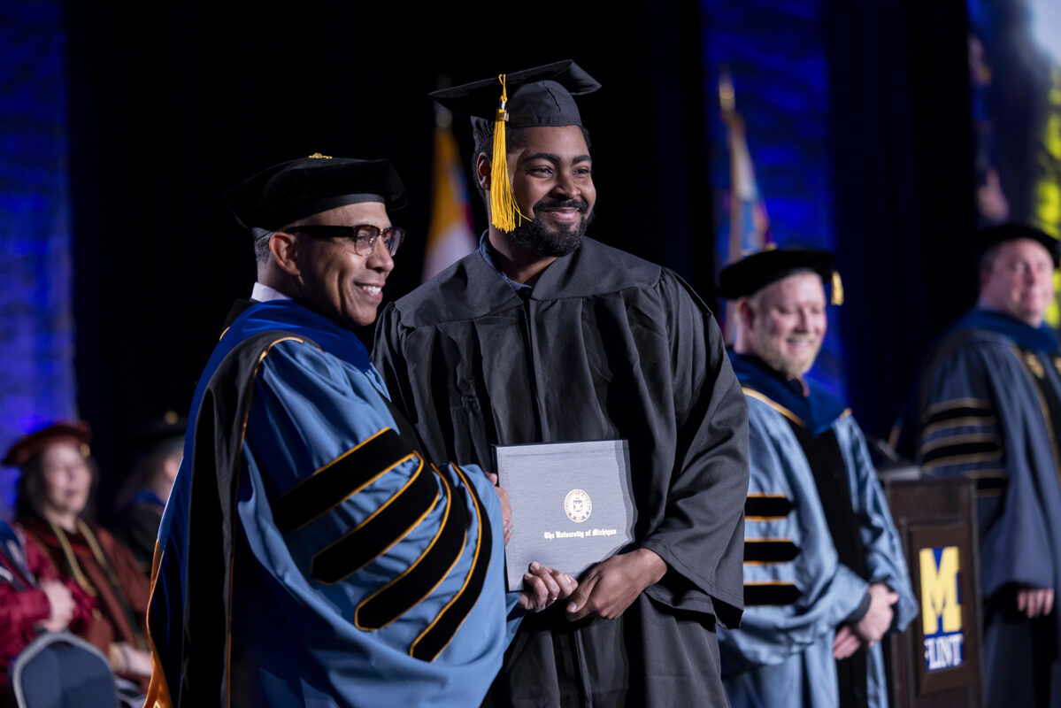 A faculty member shakes hands with a graduate holding his diploma.