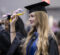 A young woman with long blonde hair in a black cap and gown smiles as she moves the tassel on her graduation cap.