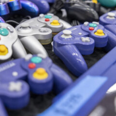 A variety of purple and silver GameCube controllers displayed on a table.