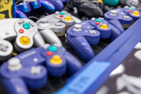 A variety of purple and silver GameCube controllers displayed on a table.