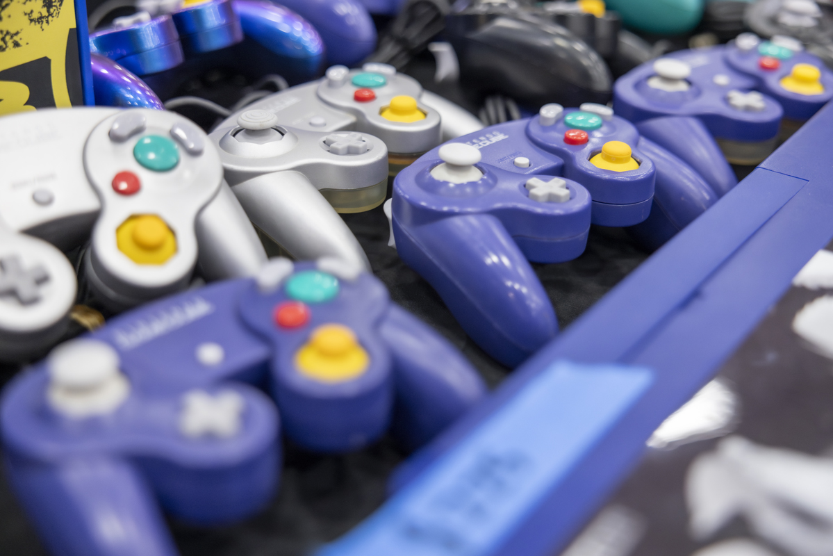 A variety of purple and silver GameCube controllers displayed on a table.