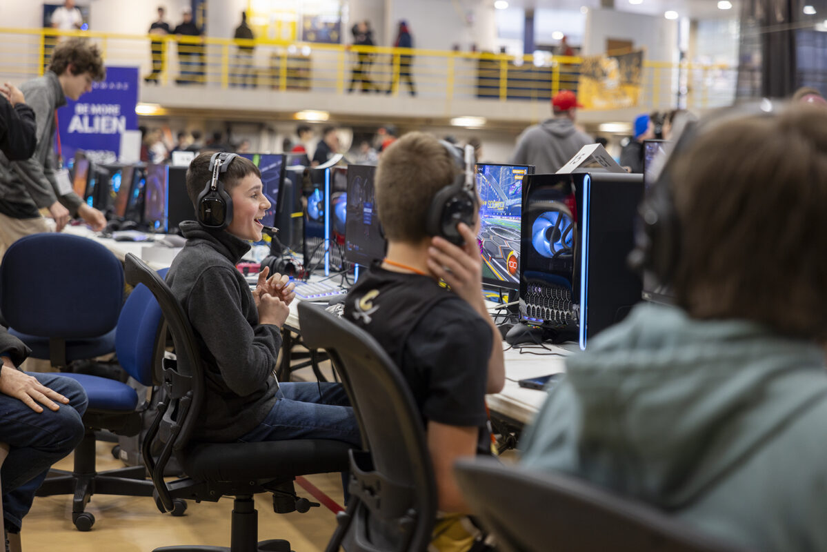 A young gamer smiles while playing a game on a PC in a tournament setting.