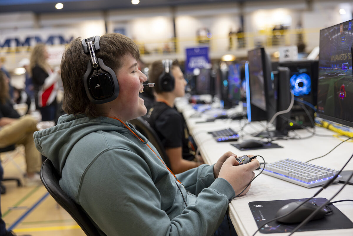 A gamer wearing a headset smiles while playing a game on a PC.