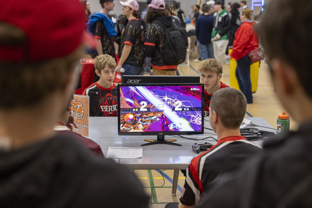 A group of players competes in a video game tournament, seated around a monitor.