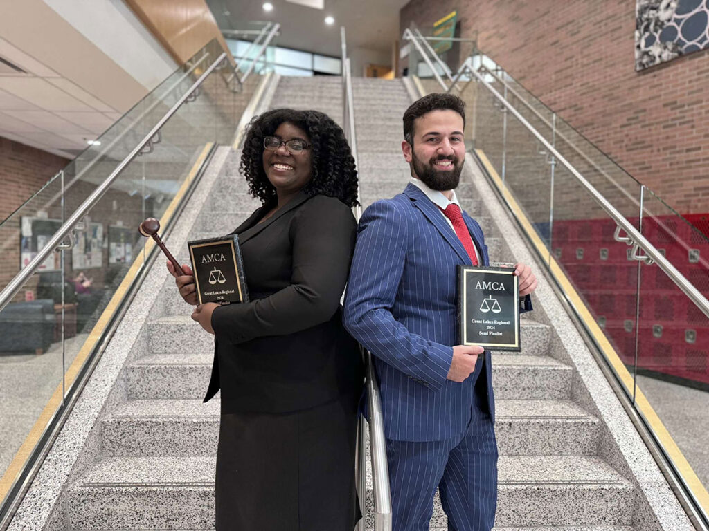 A Black female and Middle Eastern male stand back-to-back on a staircase showing off a recent award