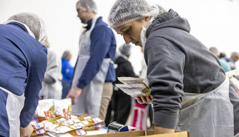 A UM-Flint volunteer in a hairnet packing food.