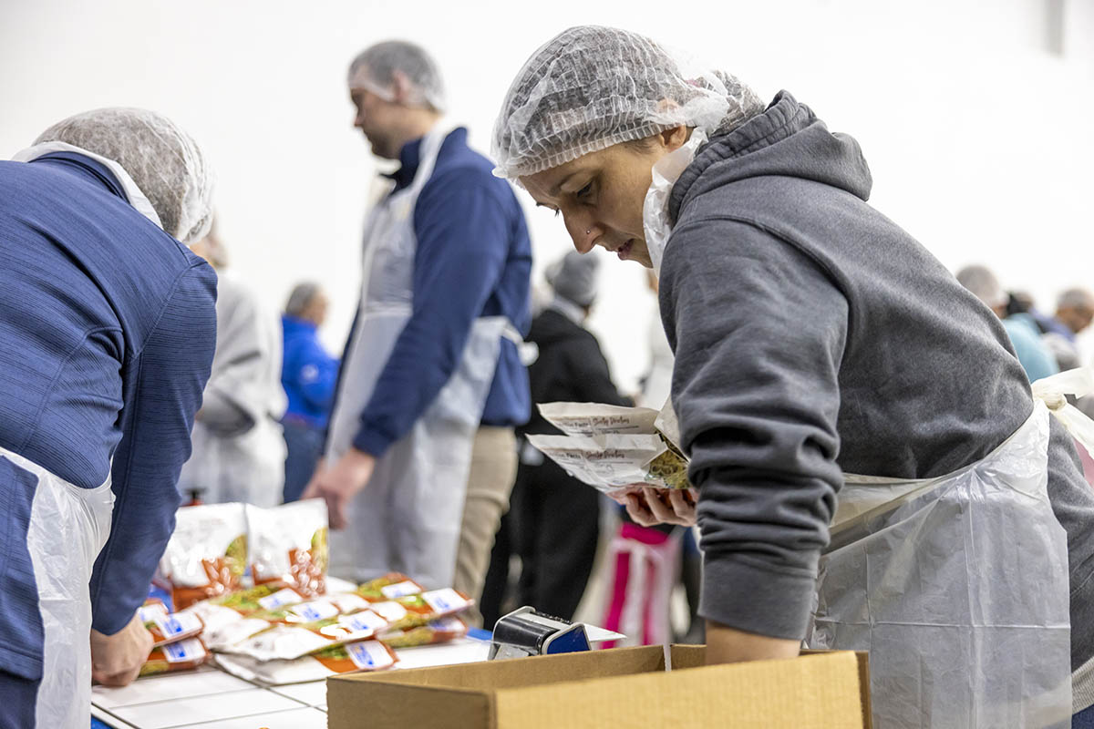 A UM-Flint volunteer in a hairnet packing food.