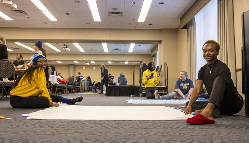 Two UM-Flint volunteers seated on the floor working on a blanket