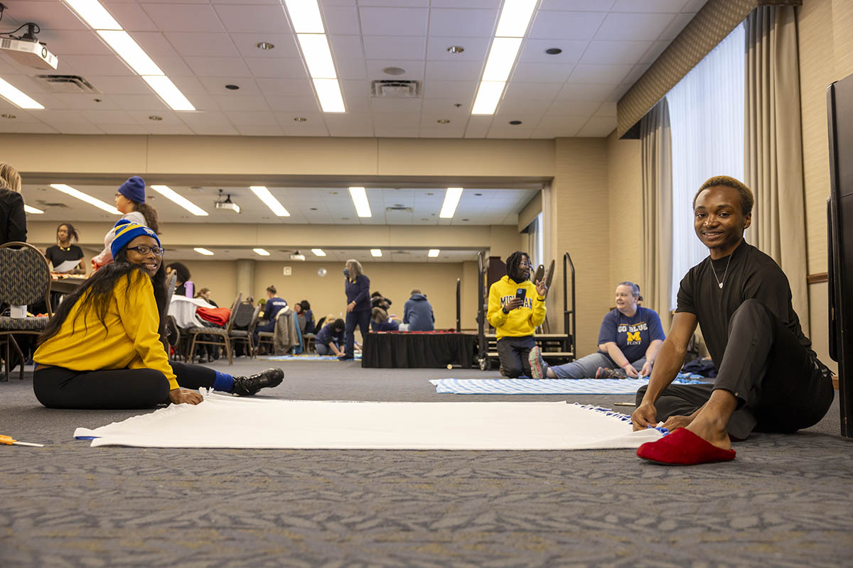 Two UM-Flint volunteers seated on the floor working on a blanket