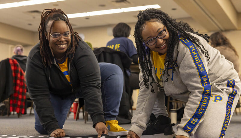 Two UM-Flint volunteers smiling while working on a blanket.